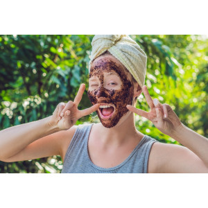 Body Scrubs. Smiling woman with coffee scrub in her face and white towel on her head.