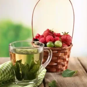 Health Embassy clear glass cup of Raspberry leaf tea next to basket of fresh berries on wooden table top view