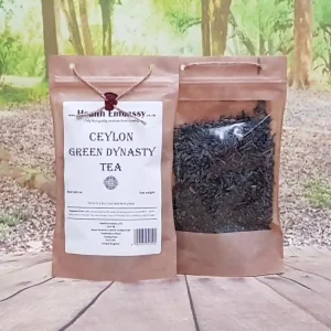 Loose leaf Ceylon Green Dynasty Tea in Health Embassy paper bag, vibrant green leaves on wooden surface
