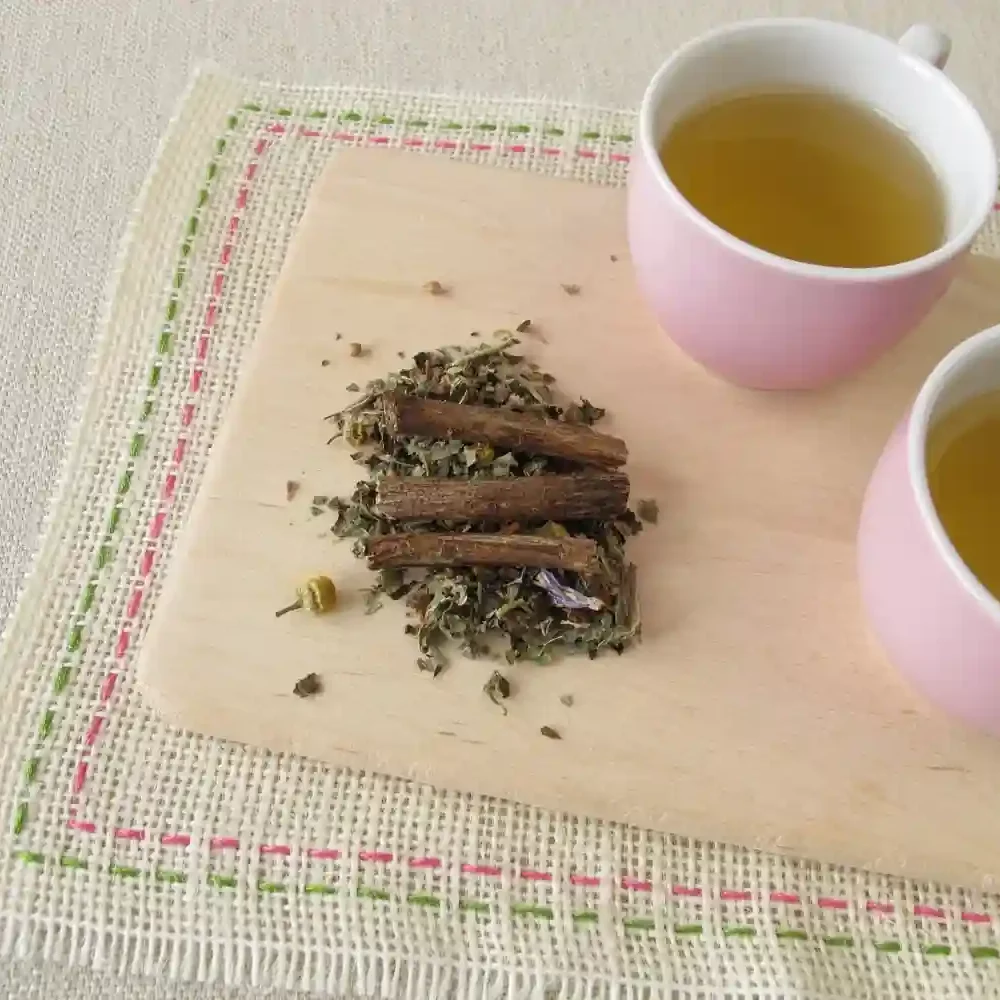 Health Embassy top view of two pink cups with tea and wooden board with dried Licorice Root and other herbs