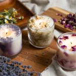 Three natural herbal candles with lavender, chamomile, and rose petals on a wooden surface, glowing softly – Health Embassy herbal candles.